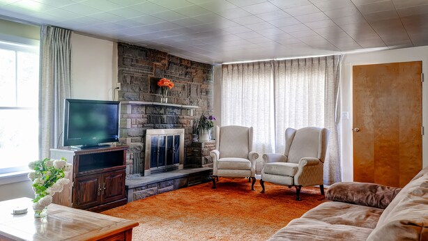 Ein Wohnzimmer mit Kamin aus Stein, einem Fernseher, zwei Sesseln und einem Sofa.