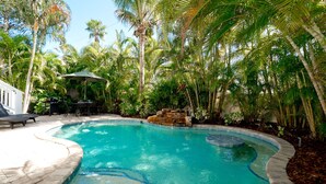 Una piscina rodeada de exuberante vegetación tropical, con un patio y una parrilla.