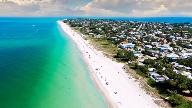 Vista aérea de una zona costera con playa, casas y aguas azul turquesa.