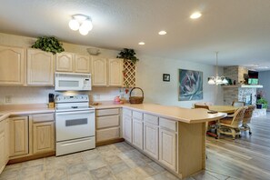 A kitchen with wooden cabinets, a microwave, an oven, a dining area with a table and chairs, and a hanging light fixture.