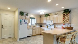 A kitchen with wooden cabinets, a central island, wicker chairs, and a refrigerator. - Tranquil Osage Beach Condo w/ Waterfront Decks! (Osage Beach)