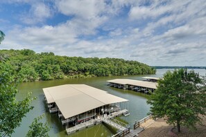 Une propriété au bord du lac, avec plusieurs bateaux amarrés, une terrasse couverte et une rive bordée d’arbres.