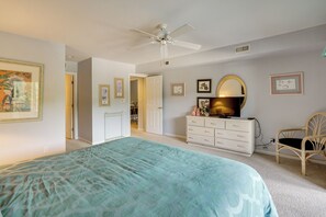 Un dormitorio con cama, ventilador de techo, cómoda, silla y cuadros en las paredes.