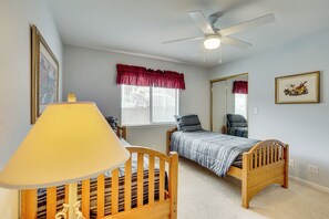 A bedroom with two single beds, a ceiling fan, a window with blinds, a lamp, and a mirror.