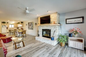 A living room with a fireplace, a ceiling fan, a television, and a dining area.