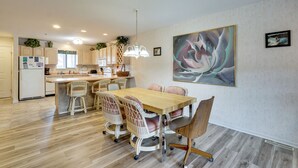 A modern kitchen with wooden cabinets, a dining area with a wooden table and wicker chairs, and a large abstract painting on the wall. - Tranquil Osage Beach Condo w/ Waterfront Decks! (Osage Beach)