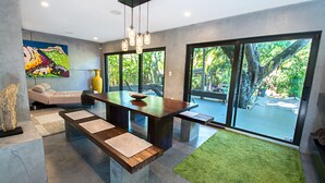 A modern dining area with a wooden table, benches, and a large window offering a view of greenery.