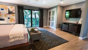 A modern bedroom with a large bed, a TV, and a balcony with a view of greenery.