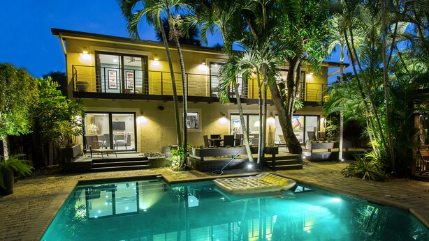 A two-story house with a swimming pool, outdoor seating, and a balcony.