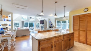 Una cocina amplia con armarios de madera, encimera de granito, iluminación colgante y ventanas grandes con vistas al exterior.