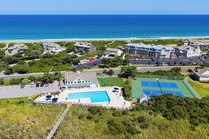 A coastal property with a large swimming pool, tennis courts, and a view of the ocean.