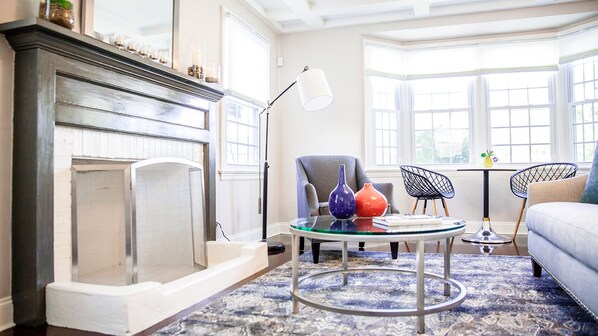 Cozy up by the fireplace in this stylish living room, featuring a comfortable sofa and a large window with a view.