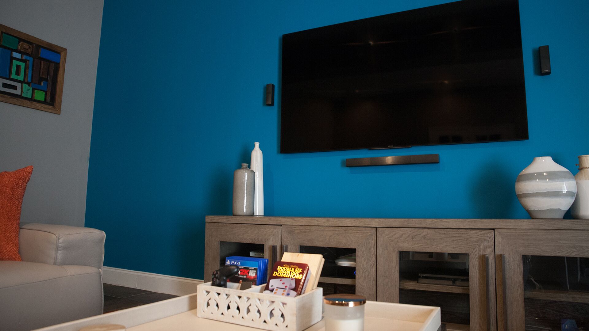 Un salon avec un mur bleu, un téléviseur à écran plat fixé au-dessus d’un meuble en bois, et une table basse blanche sur laquelle sont posés des jeux de société.