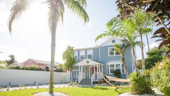 A two-story house with a front porch, a hammock, and a well-maintained lawn.