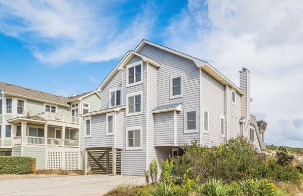 A two-story house with a gabled roof, a front porch, and a garage. - Summer Camp - Corolla, Crown Point, Oceanfront, 70 Ft to Beach, Community Pool, Hot Tub, Pets OK (Corolla)
