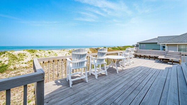 A wooden deck with white Adirondack chairs and a table overlooking a beach. - Summer Camp - Corolla, Crown Point, Oceanfront, 70 Ft to Beach, Community Pool, Hot Tub, Pets OK (Corolla)