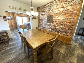 Un coin repas avec un mur en briques, une table en bois, des chaises et un lustre.