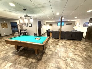 Une table de billard avec des billes, un canapé, un téléviseur et une porte.