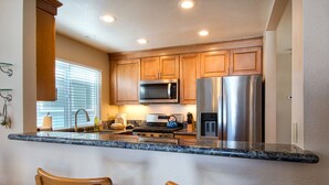 A kitchen with wooden cabinets, stainless steel appliances, granite countertops, and two wooden chairs.