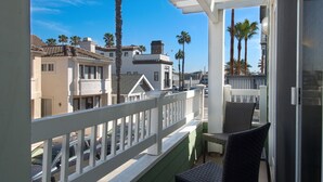 A balcony with a white railing, wicker furniture, and a view of residential buildings and palm trees.