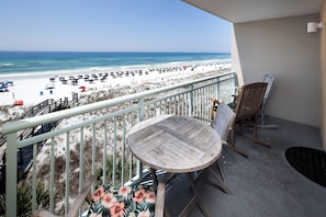 Un balcon avec vue sur la plage, une table en bois et un fauteuil Ă bascule.