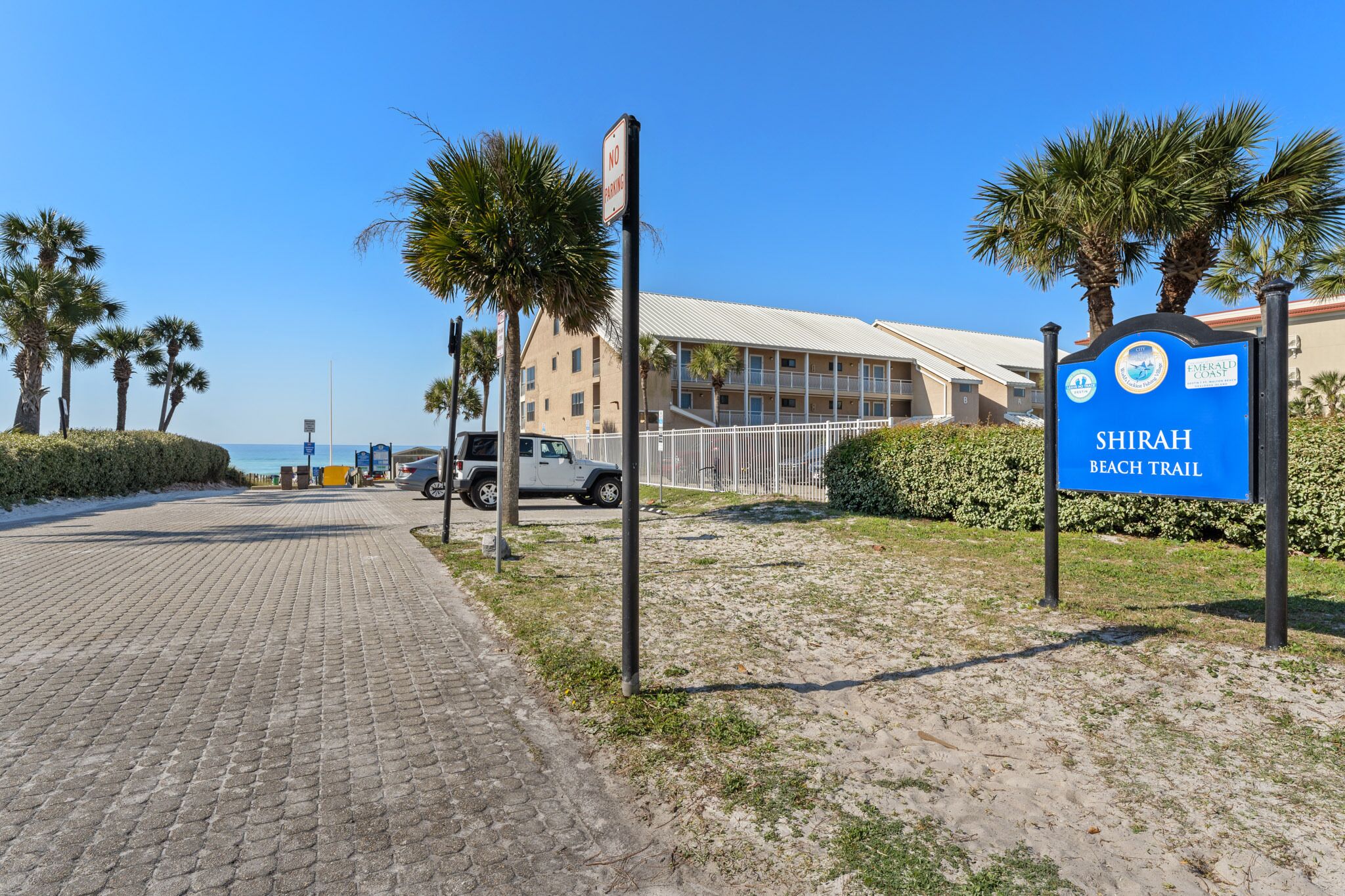 A paved pathway leading to a building with a sign reading "SHIRAH BEACH TRAIL".
