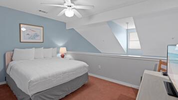Una camera da letto con un letto, una scrivania, una ventola a soffitto, una lampada e un quadro appeso al muro.