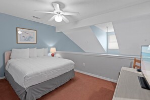 Een slaapkamer met een bed, bureau, plafondventilator, lamp en een ingelijst beeld aan de muur.