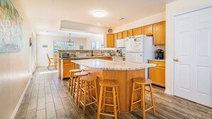 A kitchen with wooden cabinets, a large island with stools, a refrigerator, and a microwave.