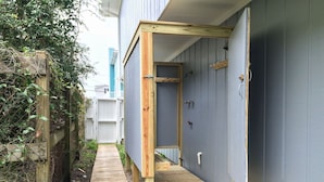 Uma passagem de madeira estreita que leva a um edifício com fachada azul e porta de madeira.