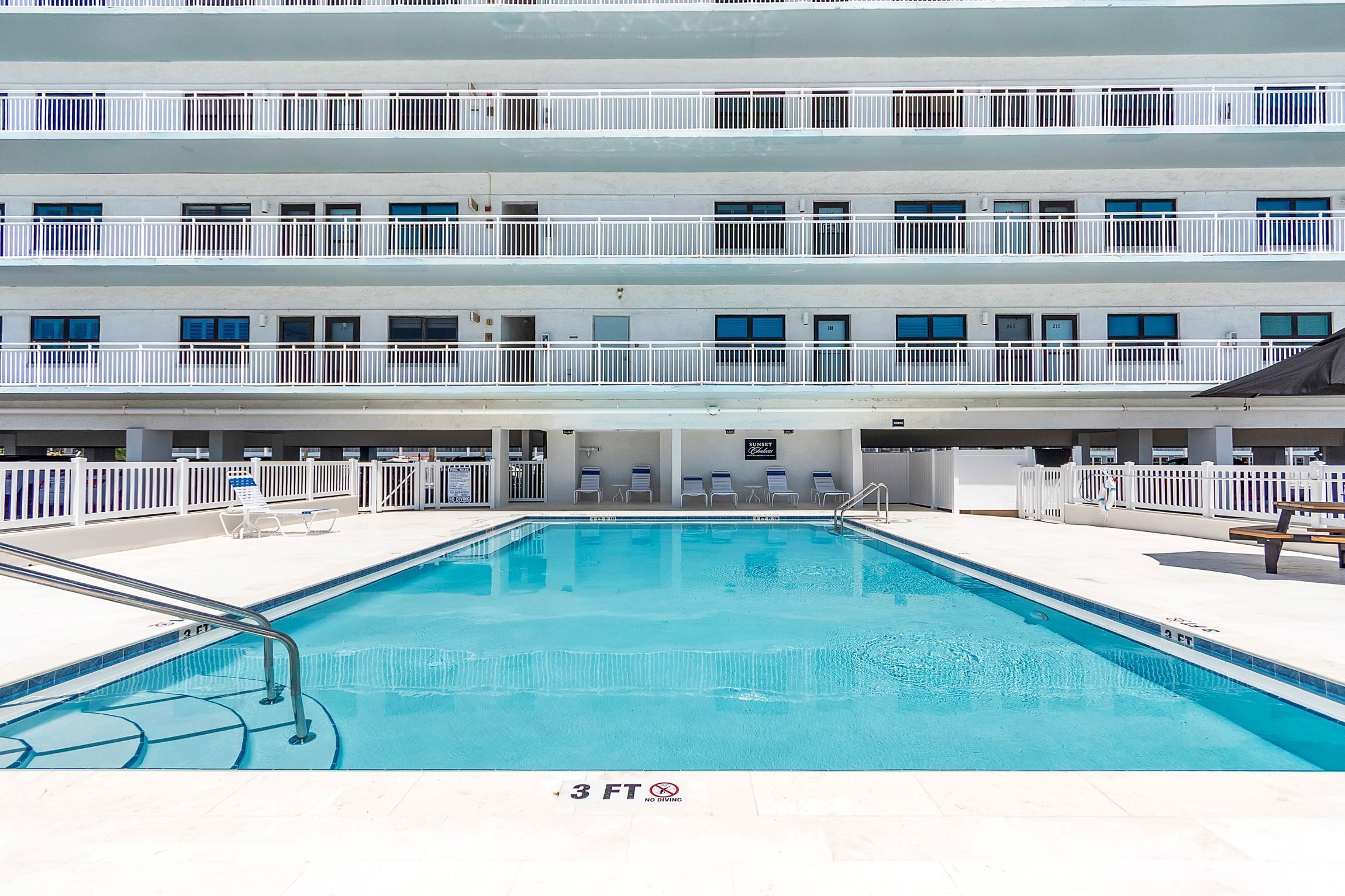 Un hotel con piscina, varios balcones y una zona para tomar el sol.