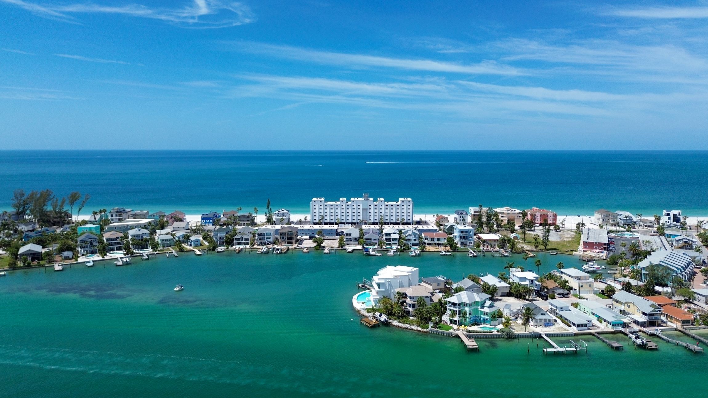 An aerial view of a coastal resort area with a large hotel, marina, and clear turquoise waters.