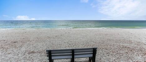 A beach with a single bench facing the ocean.