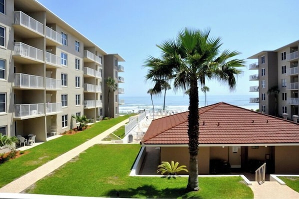 A multi-story hotel with balconies, a palm tree, and a view of the ocean.