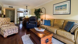 A living room with a sofa, armchair, ottoman, and a wooden chest of drawers.