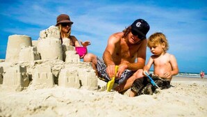 A sandy beach with a sandcastle and a child playing.