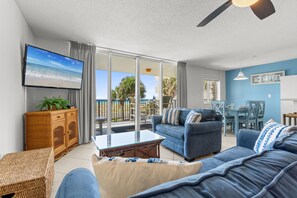 A living room with a sofa, a television, a wicker cabinet, and a glass coffee table. - DP 201: Emerald Escape - Endless Sunshine, Ocean Breezes – Your Condo Awaits! (Fort Walton Beach)