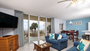 A living room with a blue sofa, a glass coffee table, a wicker side table, and a flat-screen TV.