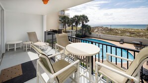 A balcony with a pool, chairs, and a view of the beach.