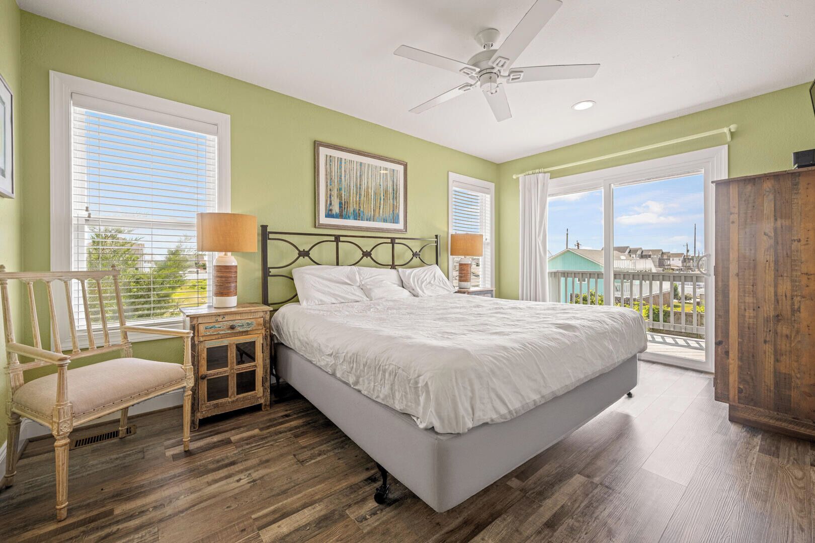 A bedroom with a bed, a chair, a nightstand, a ceiling fan, and a view of the outside.