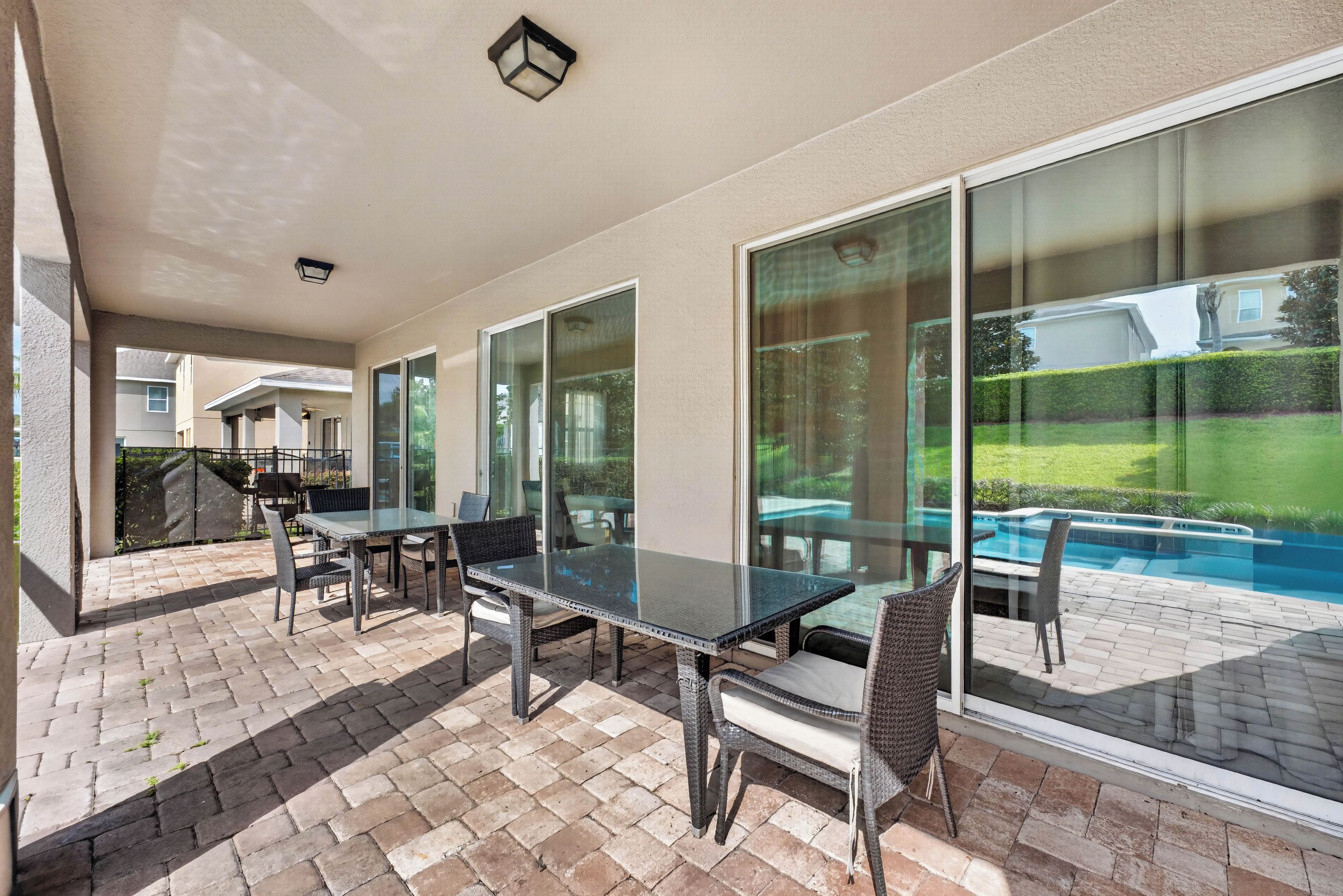 A covered patio with a glass table and chairs, a pool in the background, and a view of a residential area.