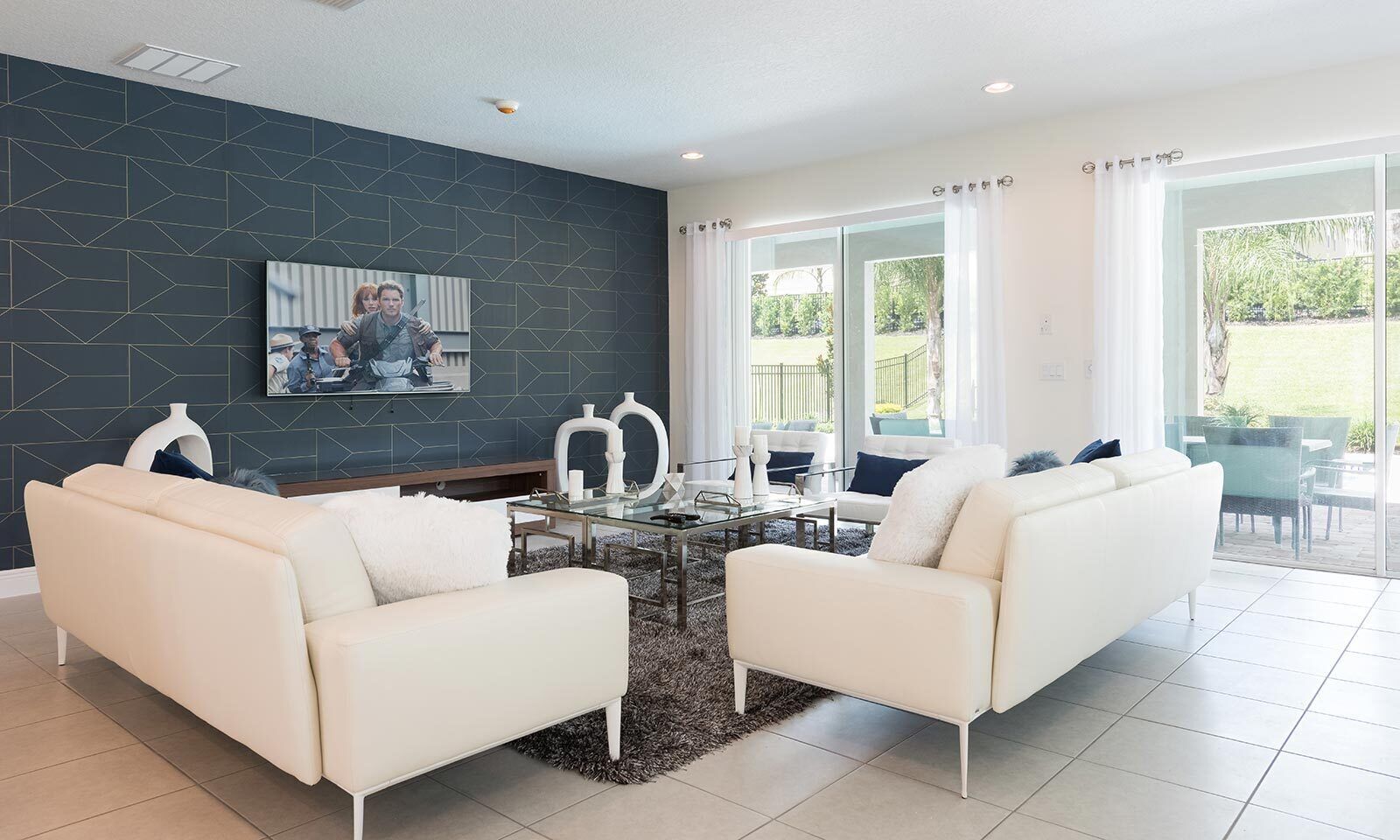 Un salon moderne avec deux canapés blancs, une table basse en verre et un mur d’accent de couleur foncée orné d’un motif géométrique.
