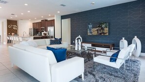 A modern living room with a white sofa, a glass coffee table, and a dark accent wall. - Stylish Sleek Home with Full Kitchen at Encore (Kissimmee)