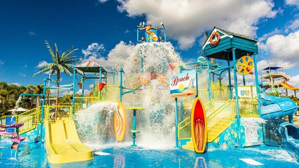 A water park with multiple slides and water features, including a large water fountain and a sign that reads "Beach". - Stylish Sleek Home with Full Kitchen at Encore (Kissimmee)