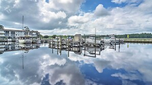 A marina with boats docked, a building with a balcony, and a clear sky with clouds. - Ocean Springs Condo in Waterfront Resort! (Ocean Springs)