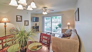 A living room with a sofa, dining table, and chairs, a ceiling fan, and a view through a glass door to an outdoor area. - Ocean Springs Condo in Waterfront Resort! (Ocean Springs)