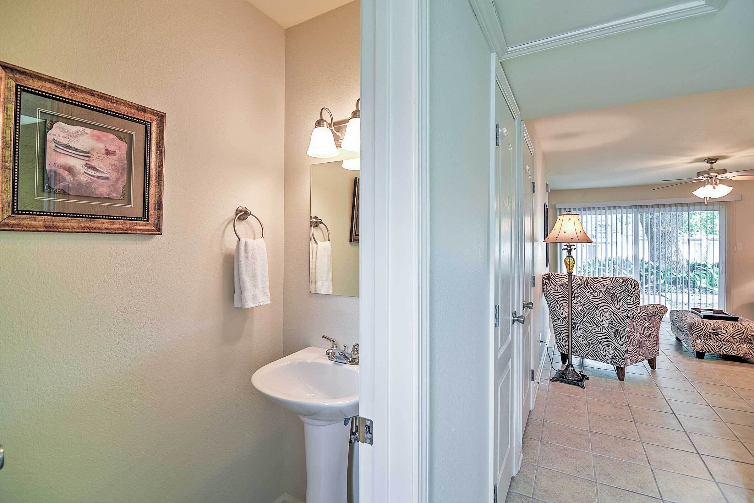 A bathroom with a sink, mirror, and towel rack. There is a chair and a lamp in the adjacent living area.