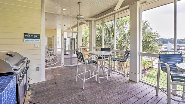 A covered outdoor area with a barbecue grill, seating, and a view of palm trees. - Ocean Springs Condo in Waterfront Resort! (Ocean Springs)