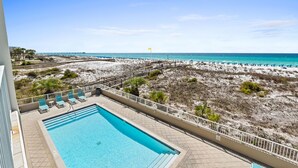 Une piscine avec des chaises longues, une vue sur la plage et une jetée visible au loin.