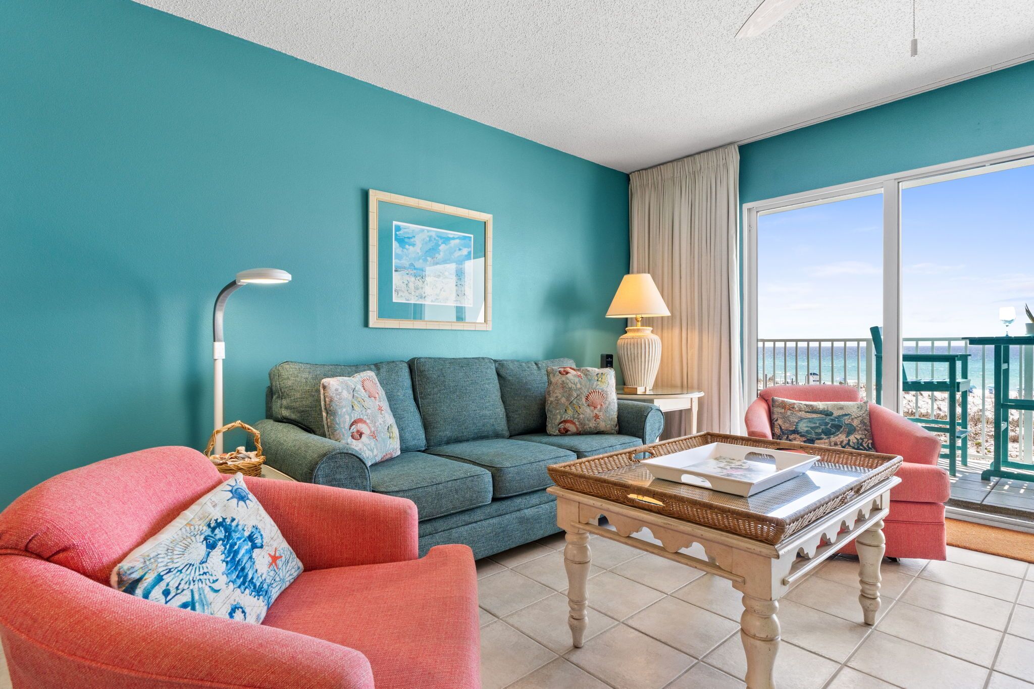 Un salon aux murs de couleur turquoise, avec un canapé, un fauteuil, une table basse et un balcon offrant une vue agréable.